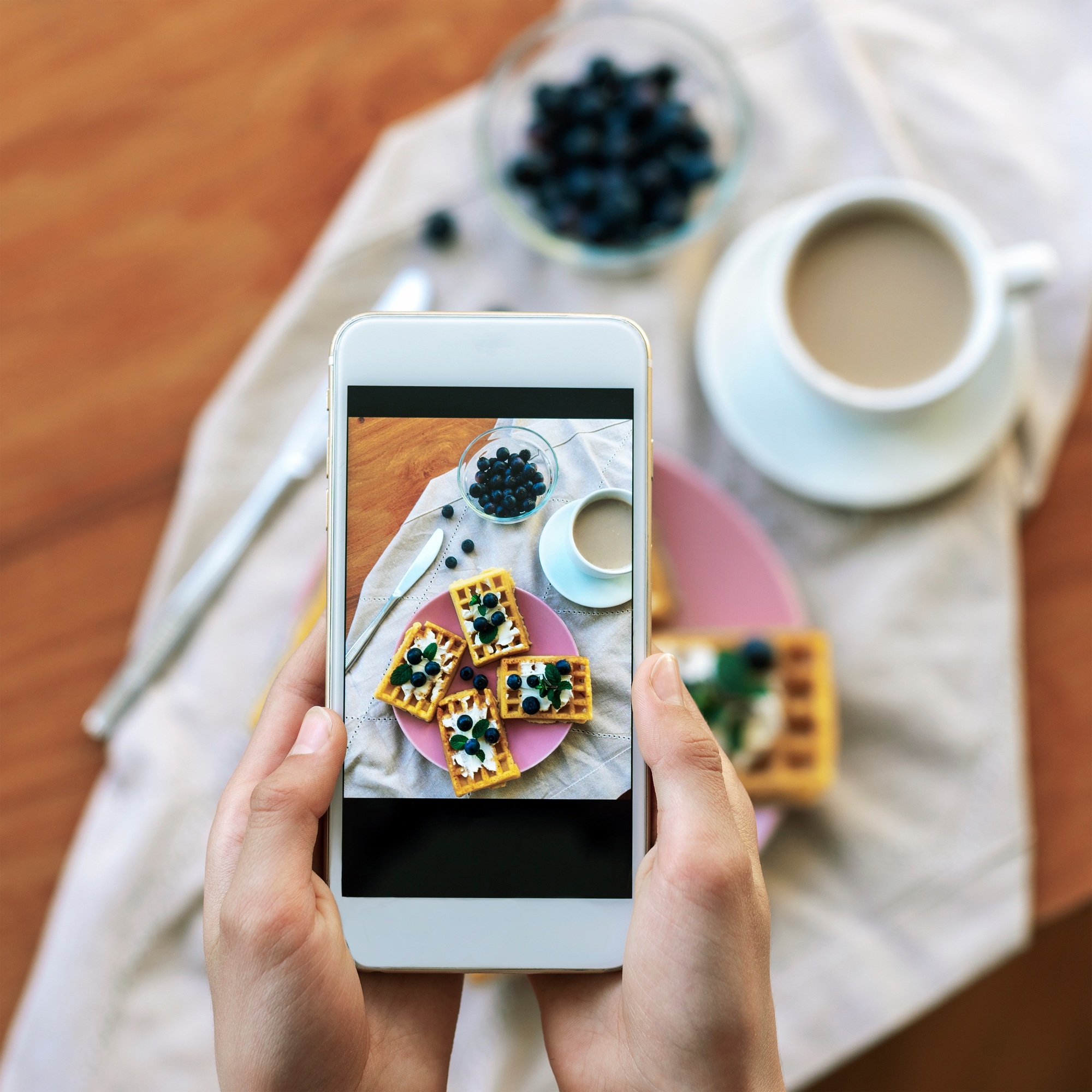 Girl's hands taking pictures of healthy waffles with blueberries by phone, top view